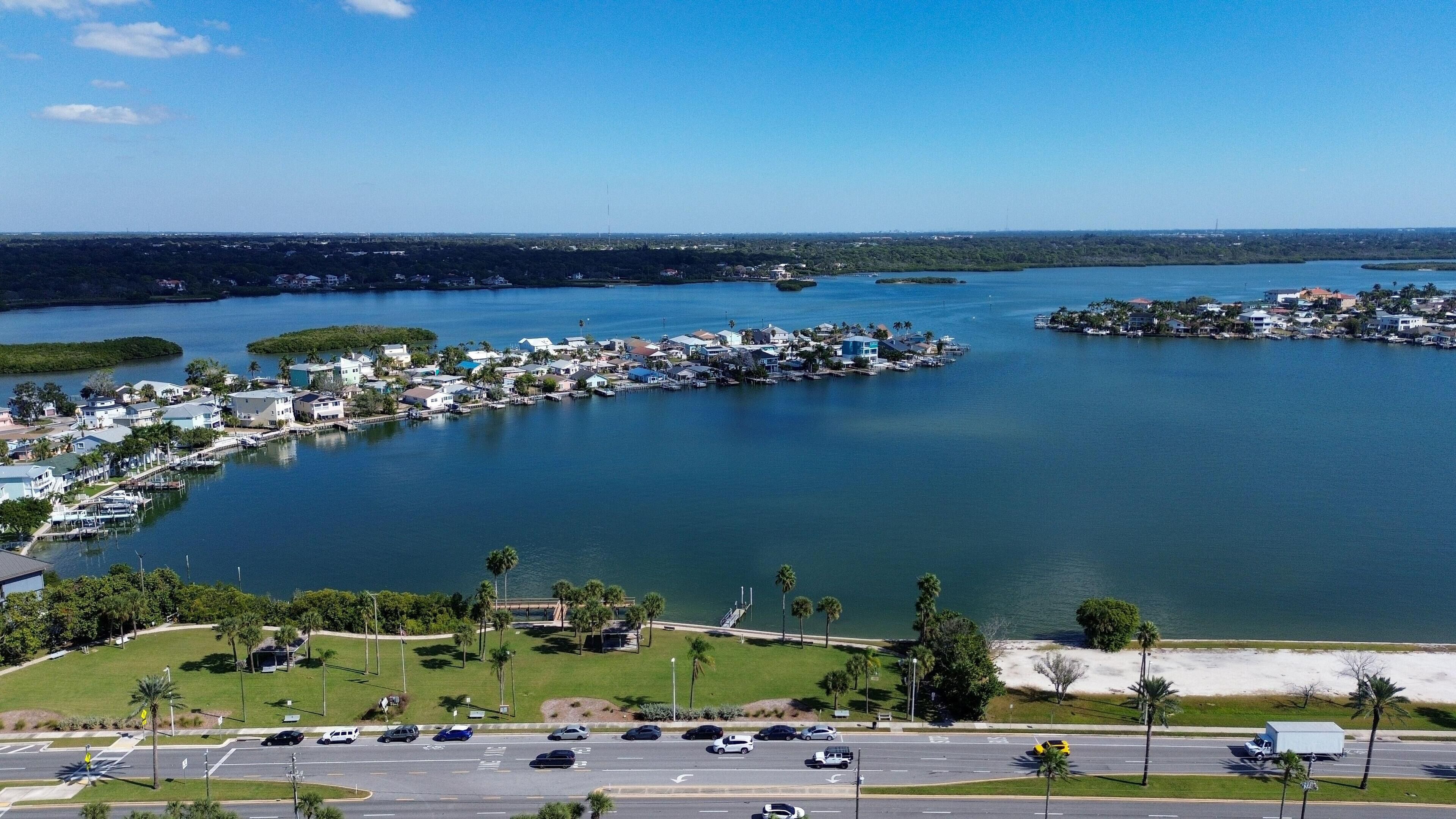 An aerial view of a coastal town with marina, residential buildings, and a road with vehicles.