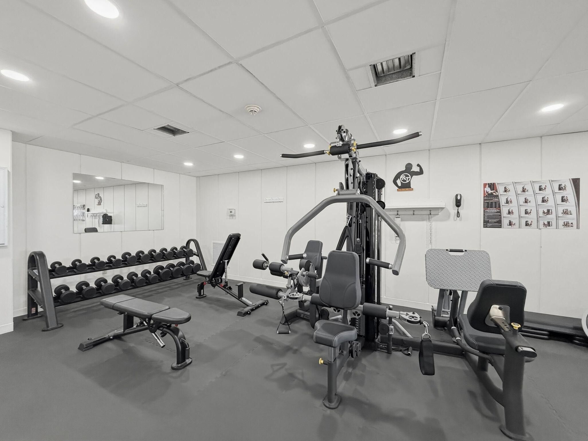 Academia com diversos equipamentos de exercício, um banco e halteres.