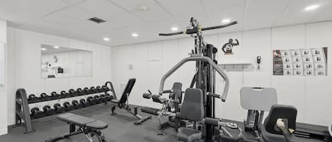 A gym with various exercise equipment, a bench, and dumbbells.