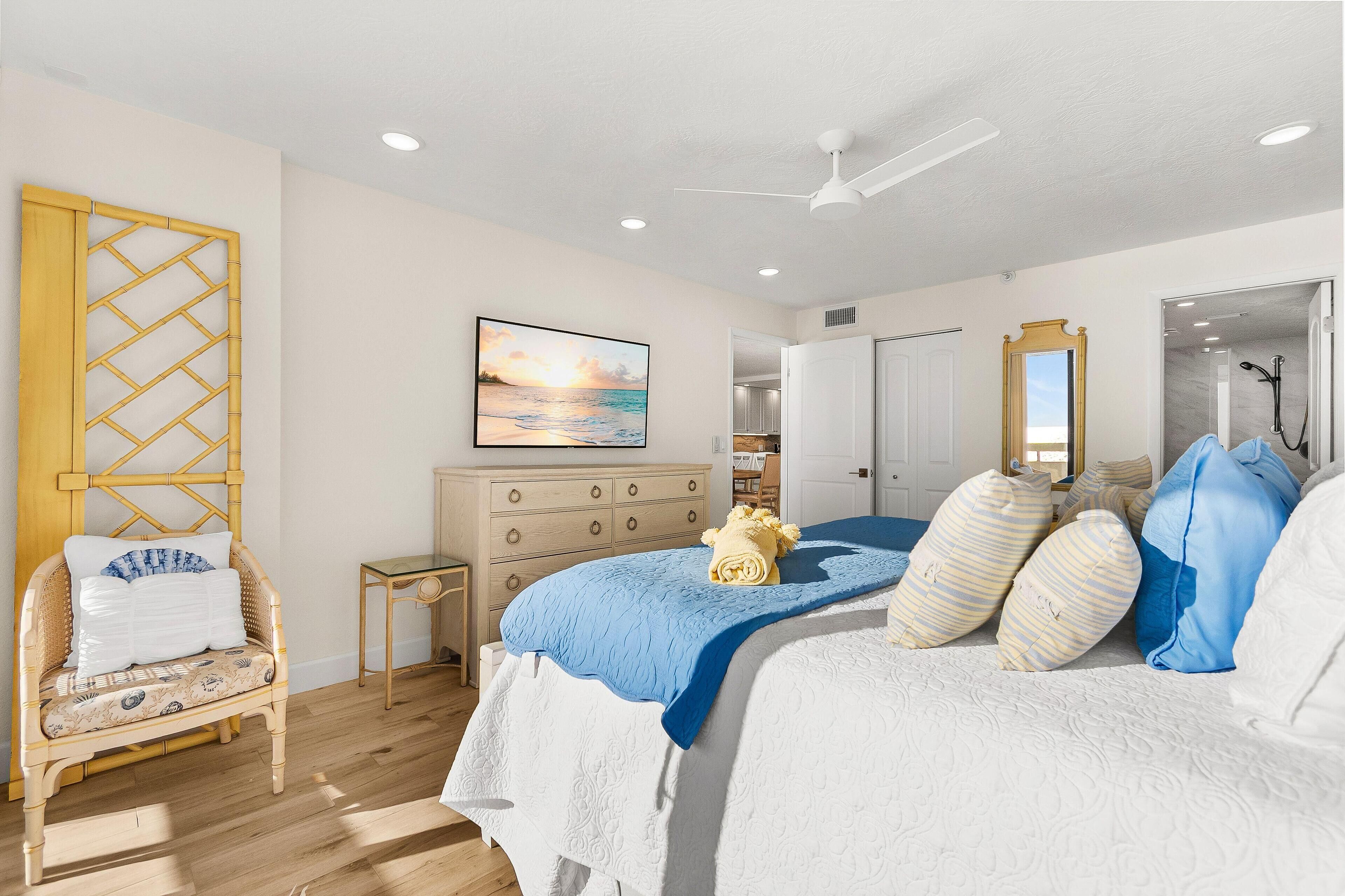 A bedroom with a bed, a chair, a dresser, a mirror, and a ceiling fan.