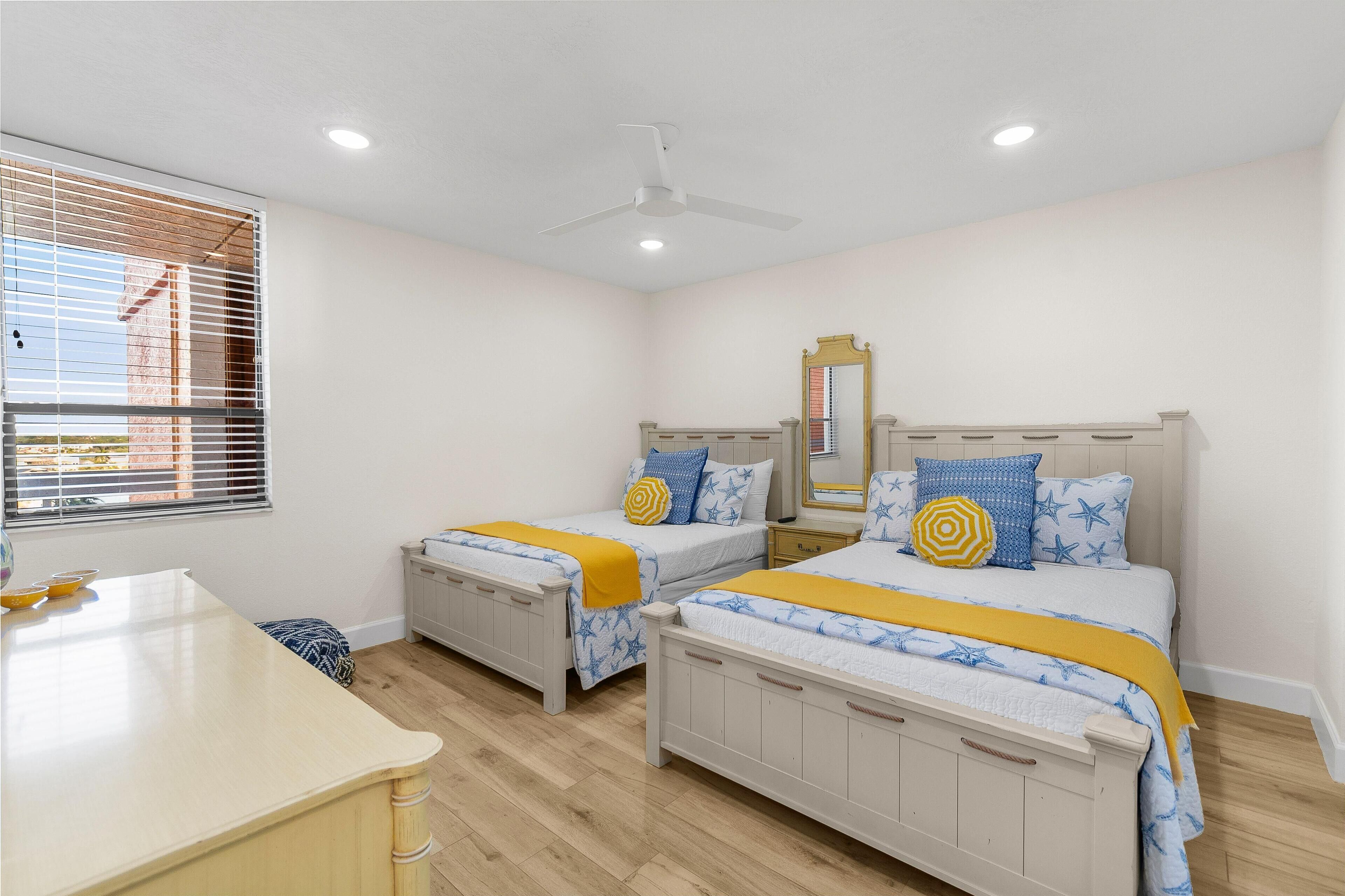A bedroom with two beds, a bedside table, a mirror, and a window with blinds.