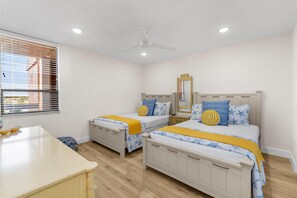 A bedroom with two beds, a bedside table, a mirror, and a window with blinds. - Redington Towers 7D (Redington Shores)