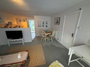 Ein kompakter Wohnraum mit Küchenzeile, Essbereich mit Tisch und Stühlen, Fernseher und einer Tür.
