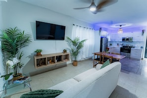 A modern living room with a sofa, TV, and dining area. A kitchen is visible in the background with cabinets and appliances. - Villa Verde - Scenic Views of El Yunque Rainforest (Río Grande)