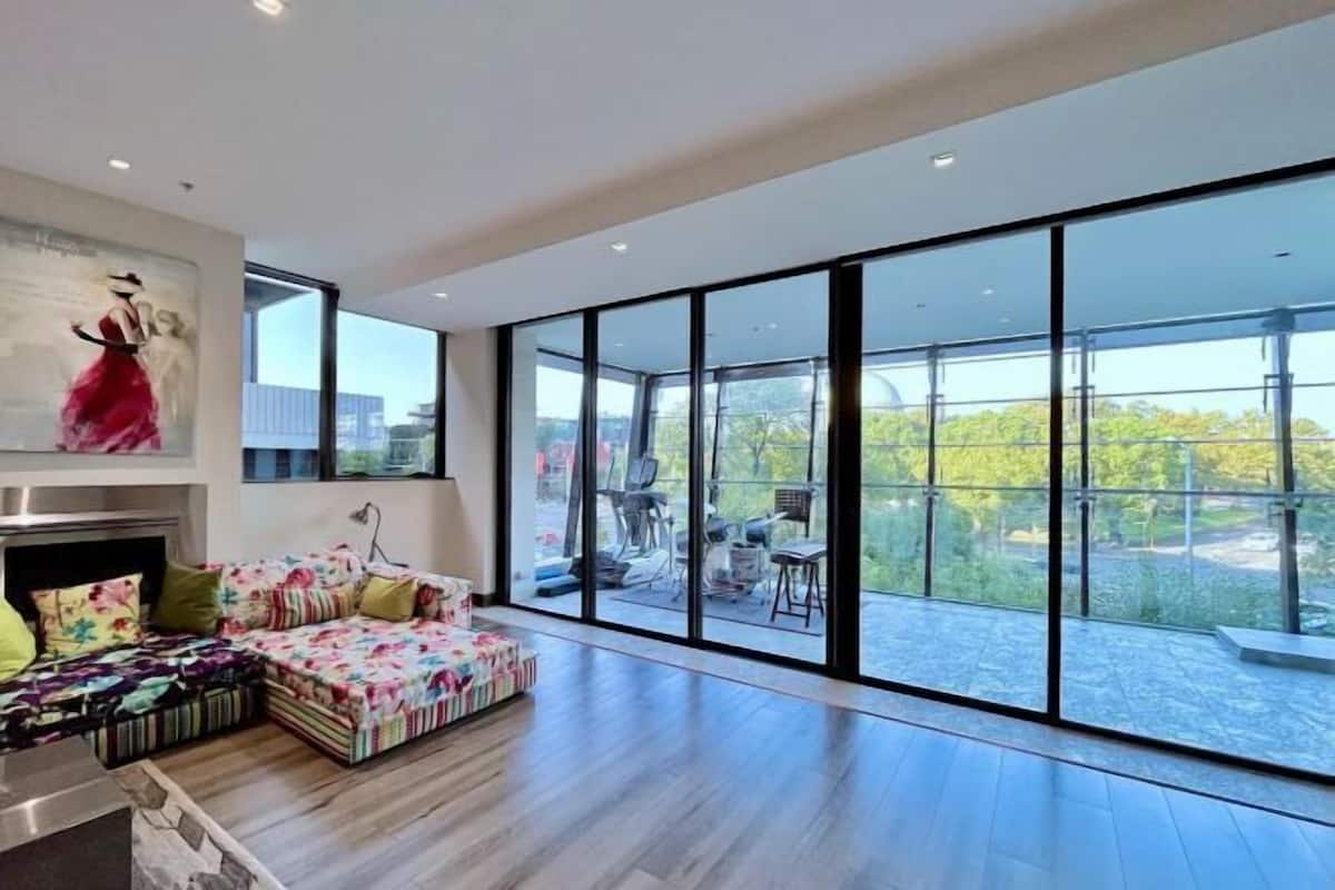 A spacious living area with a large glass wall, a sofa with colorful cushions, and a painting on the wall.