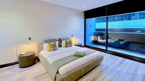 Quarto moderno com uma cama grande, abajures, uma mesa de cabeceira e vista através de uma janela ampla.