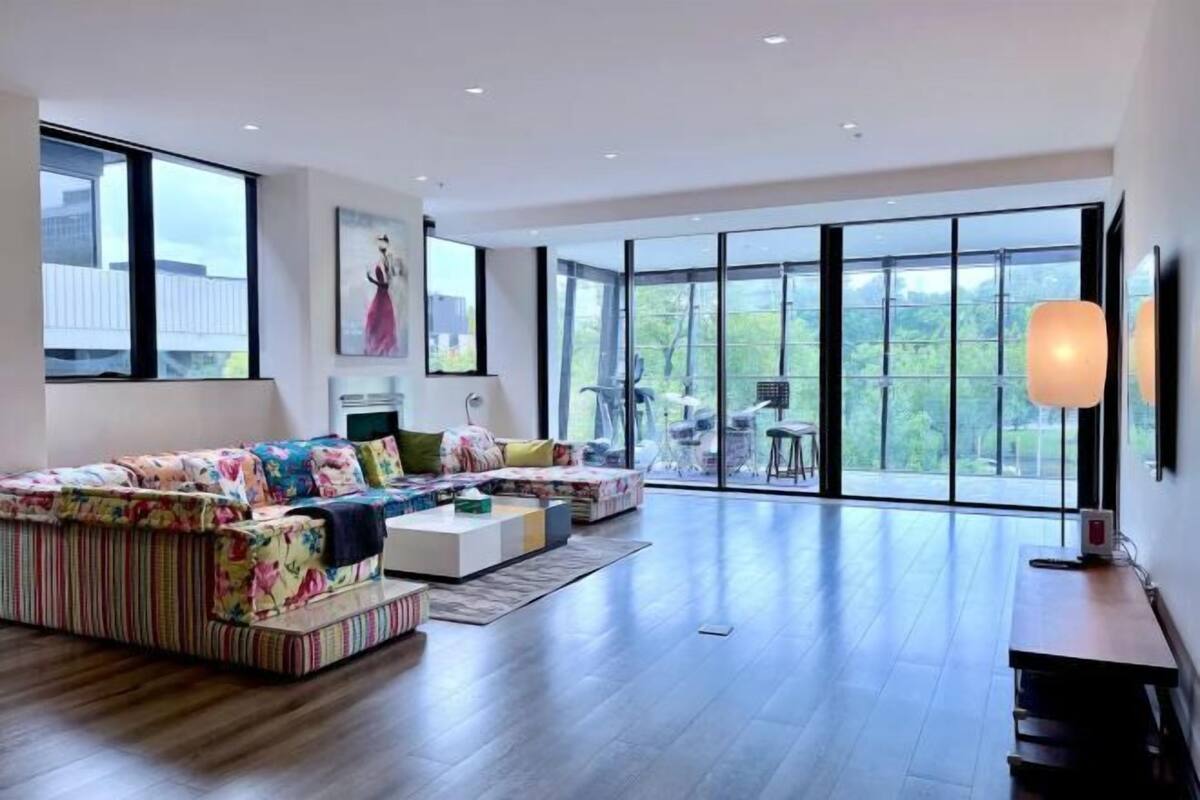 Een moderne woonkamer met een grote bank, een salontafel en een eethoek met stoelen. Een groot raam biedt uitzicht op de omgeving.