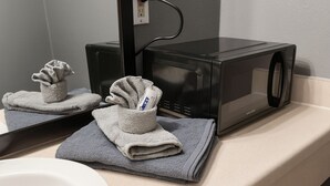 Une salle de bain avec un micro-ondes noir posé sur un comptoir beige, un miroir et des serviettes.