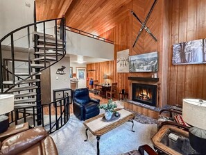 A wooden interior with a spiral staircase, a fireplace, leather furniture, and a dining area. - Mountain Condo | Pool & Hot Tub | Perfect Location (Whitefish)