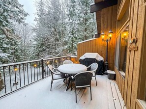 A wooden deck with a round table and chairs, a barbecue grill, and a 'Welcome' sign. - Mountain Condo | Pool & Hot Tub | Perfect Location (Whitefish)