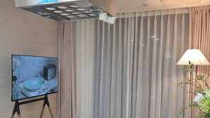 Een moderne kamer met een flatscreen televisie op een standaard, een ingebouwde kookplaat en dunne gordijnen.