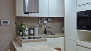 Een moderne keuken met witte kasten, een roestvrijstalen afzuigkap, een inbouwoven en een klein eiland met barstoelen.
