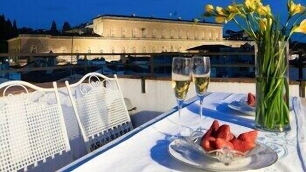 A dining table with a white tablecloth, two glasses of white wine, a plate with strawberries, and a vase with yellow flowers. - Pitti Luxury Terrace by Mmega (Florence)