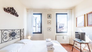 A hotel room with a bed, a desk with a computer, two windows, and a radiator. - Pitti Luxury Terrace (Florence)