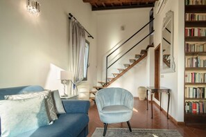 A living room with a blue sofa, a chair, a lamp, a staircase, and a bookshelf. - Pitti Luxury Terrace (Florence)