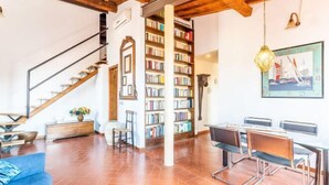 A spacious living area with a wooden staircase, a bookshelf, a dining table with chairs, and a large window. - Pitti Luxury Terrace by Mmega (Florence)