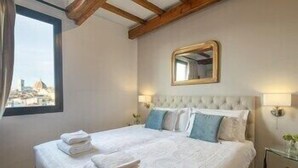 A hotel room with a bed, a window with a city view, a mirror, and a nightstand. - Pitti Luxury Terrace by Mmega (Florence)