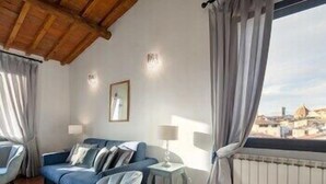 A room with a blue sofa, a small table, a lamp, and a view of a cityscape through a window. - Pitti Luxury Terrace by Mmega (Florence)