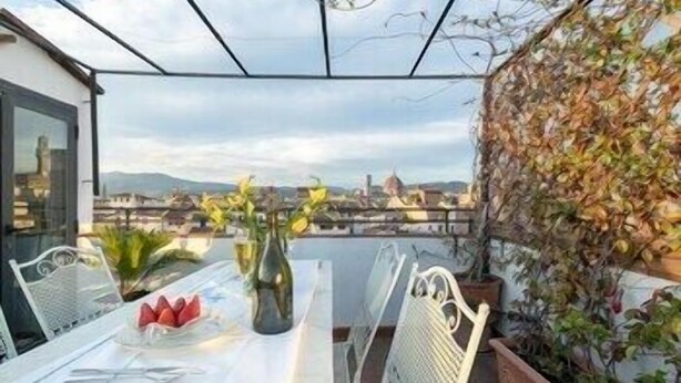 A terrace with a table set for dining, a vase with flowers, and a view of a cityscape. - Pitti Luxury Terrace (Florence)