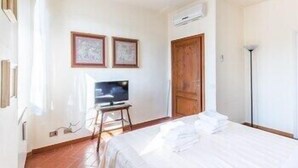 A hotel room with a bed, a television on a stand, a wooden door, and framed pictures on the wall. - Pitti Luxury Terrace (Florence)
