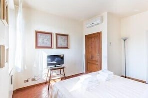 A hotel room with a bed, a television on a stand, a wooden door, and framed pictures on the wall. - Pitti Luxury Terrace (Florence)