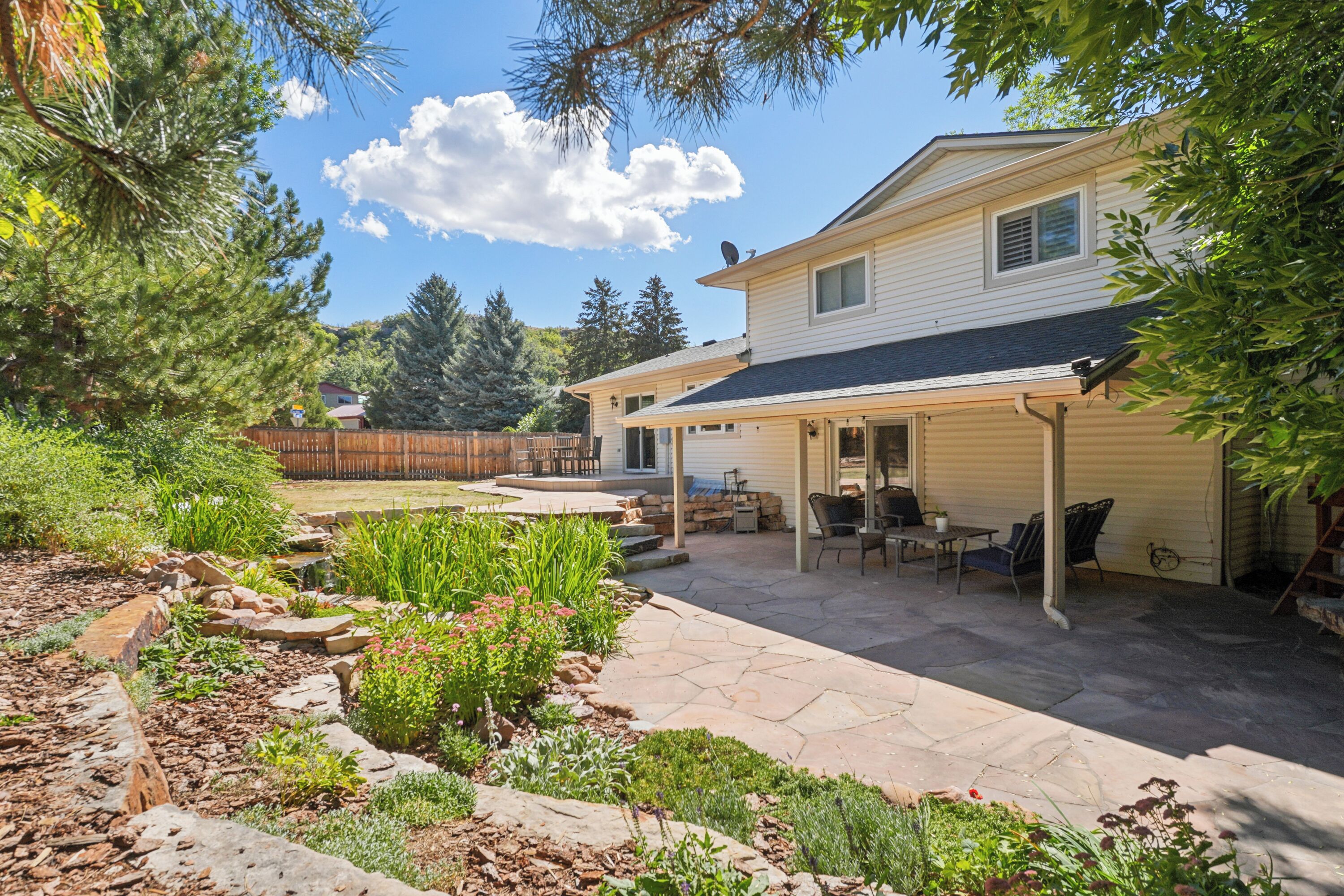 A two-story house with a covered patio area, a garage, and a landscaped garden with various plants and a small pond.