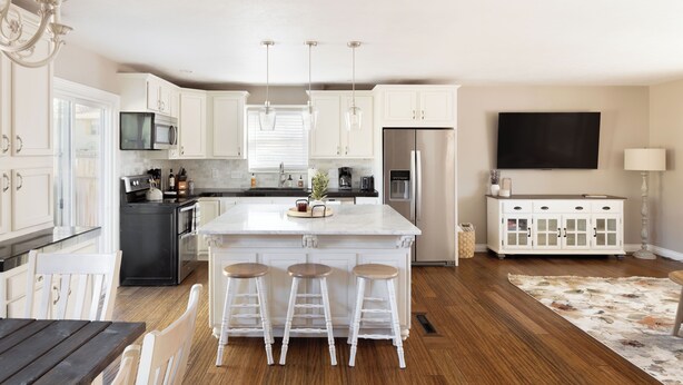 A modern kitchen with white cabinetry, a central island with stools, a black refrigerator, and a TV mounted on the wall. - The Rustic Retreat (Castle Rock)