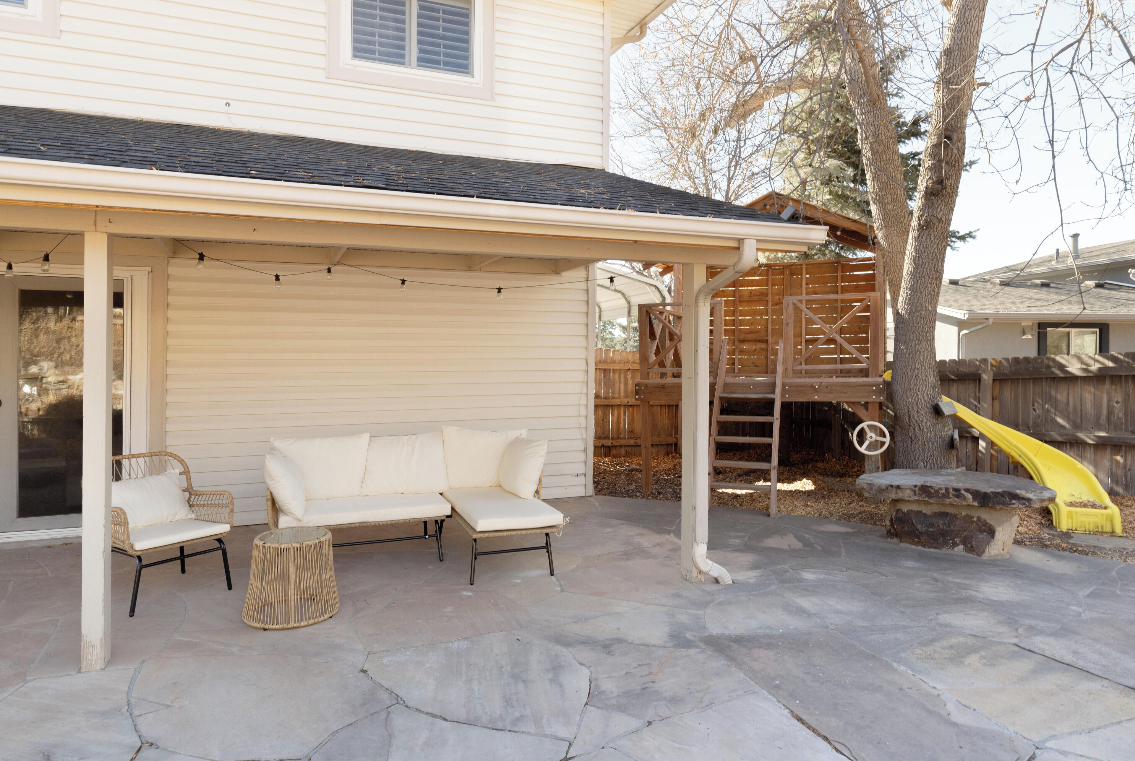 A covered patio area with a white sofa, two chairs, and a small round table.