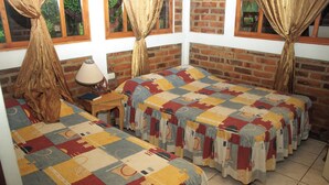 A room with two beds, a wooden nightstand, a lamp, and a window with curtains. - Colonial-Styled Hotel Villa in Ataco at 1,200 AMSL - 12 Rooms & Cabins available (Concepción de Ataco)