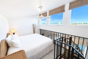 Un dormitorio con cama, mesita de noche, lámpara, ventana con vistas y barandilla de balcón.