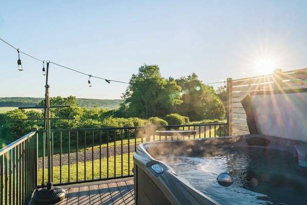 A hot tub on a deck with a view of a forest and hills.