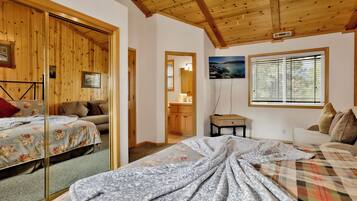 Une pièce chaleureuse avec des murs et un plafond en bois, un lit avec une literie à motifs floraux, un canapé, une petite table et une fenêtre avec des stores.