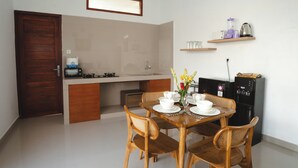 A compact kitchen with a dining table set for four, wooden chairs, a built-in stove, and a refrigerator. - Villa Taman Bali 6 (Kerobokan)