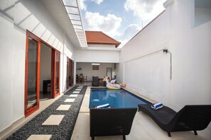 Une piscine dotée de chaises longues et d’un jouet flottant, entourée d’un patio couvert avec un sol carrelé et une vue sur le ciel.
