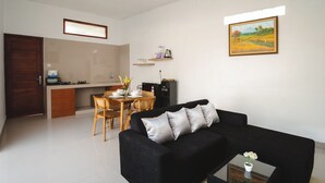 A modern living room with a black sofa, a dining table with chairs, a kitchen area, and a painting on the wall. - Villa Taman Bali 6 (Kerobokan)