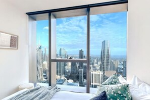 Ein Schlafzimmer mit großem Fenster, einem Bett mit Kissen und Blick auf die Stadt.