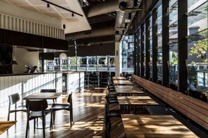 Un restaurant moderne avec un long comptoir, des tables en bois et de grandes fenêtres.