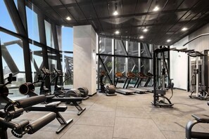 Une salle de sport équipée de divers appareils d’exercice, dotée de grandes fenêtres et présentant un design moderne.