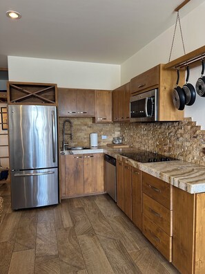 Eine moderne Küche mit Holzschränken, einem Edelstahlkühlschrank, einer Stein-Spritzschutzwand und einer hängenden Küchenutensilienstange.