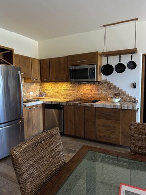 A modern kitchen with wooden cabinets, a stainless steel refrigerator, a microwave, and hanging pots. - Hello Sunshine (El Tezal)