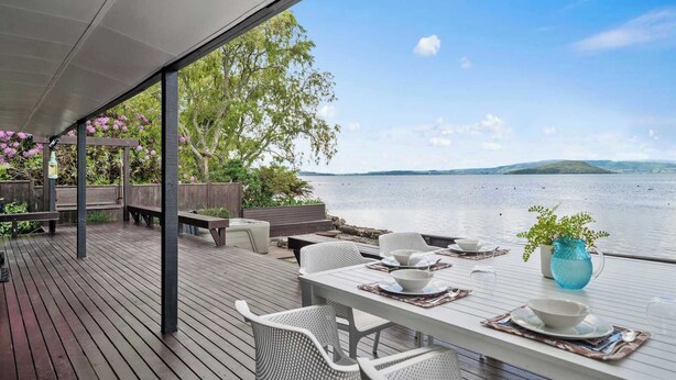 Une terrasse extérieure avec une table dressée pour le repas, donnant sur un lac paisible et sur des collines lointaines.