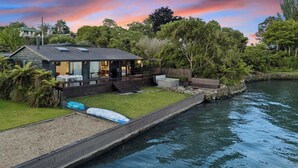 Une maison moderne dotée d’une terrasse donnant sur une étendue d’eau paisible, le tout entouré d’une végétation luxuriante.