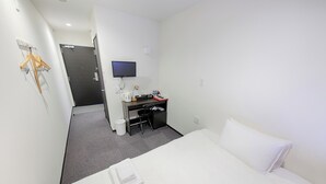 Ett hotellrum med en säng, ett skrivbord, en stol, en tv och en klädställning.