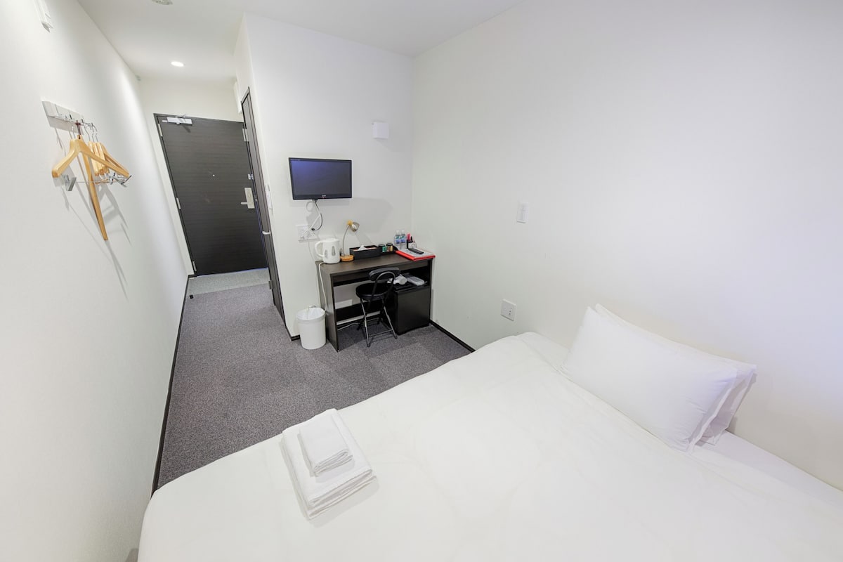 Ein Hotelzimmer mit Bett, Schreibtisch, Stuhl, Fernseher und Kleiderhaken.