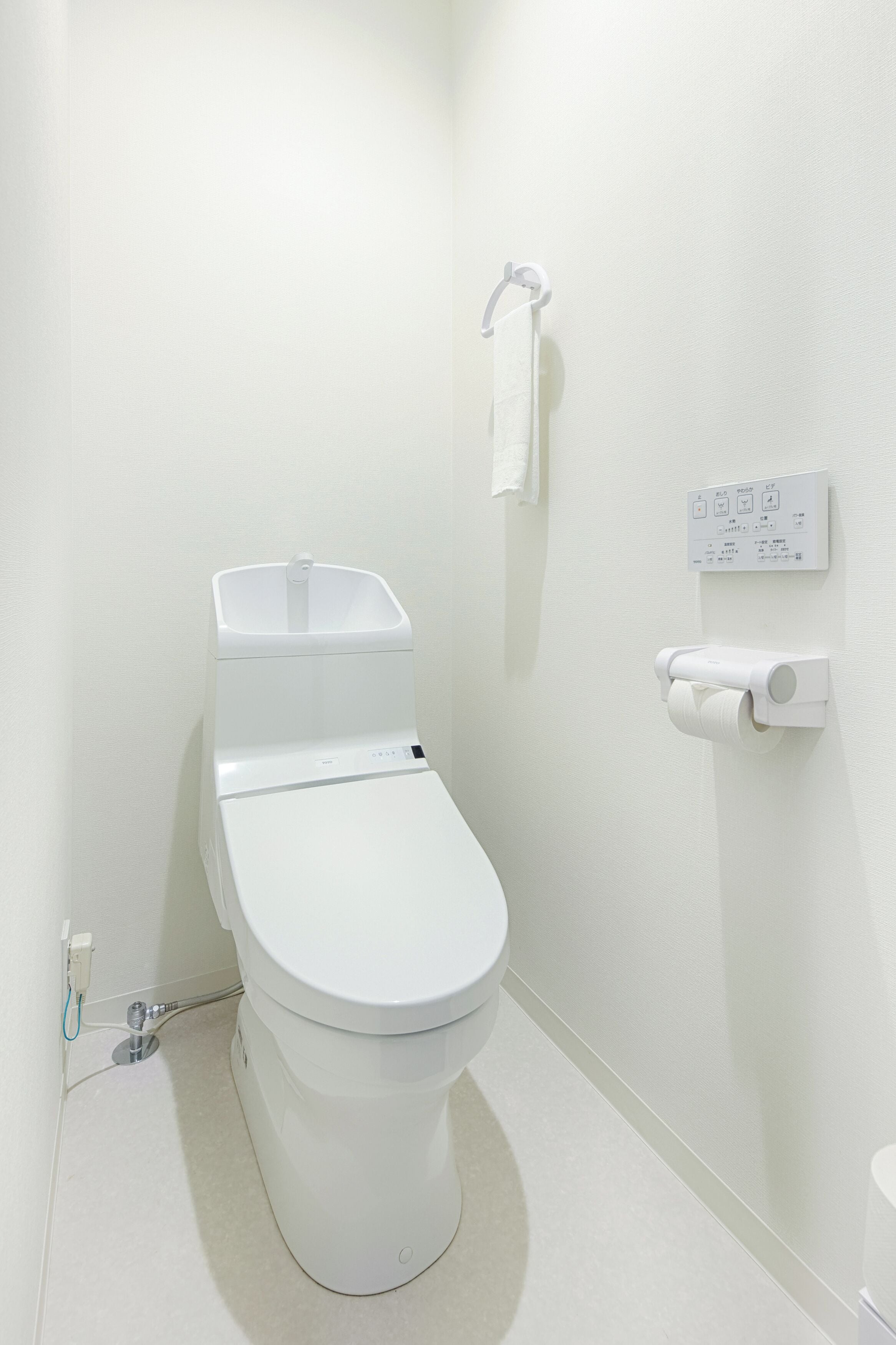 Un inodoro moderno con un panel de control, un dispensador de papel higiénico y una toalla colgada en la pared.