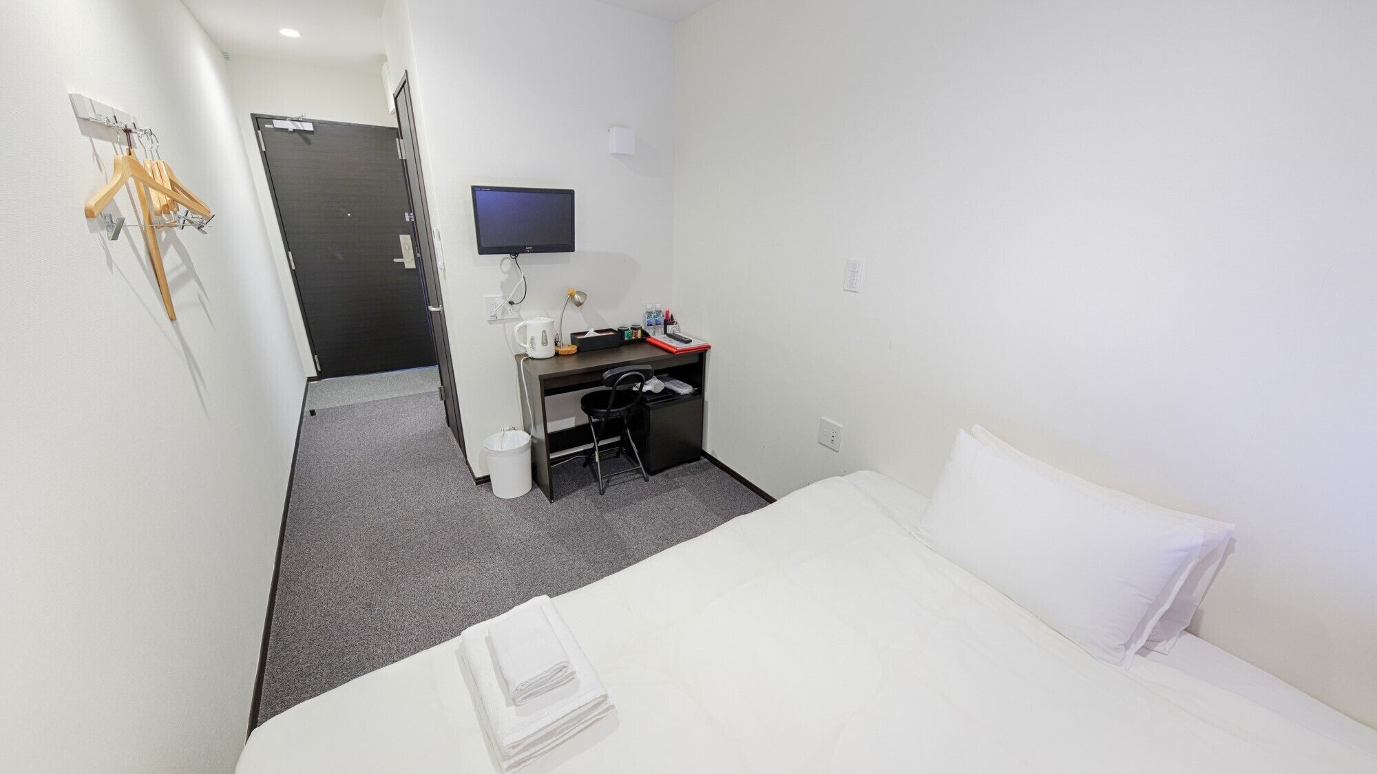 Ein Hotelzimmer mit Bett, Schreibtisch, Stuhl, Fernseher und Kleiderhaken.
