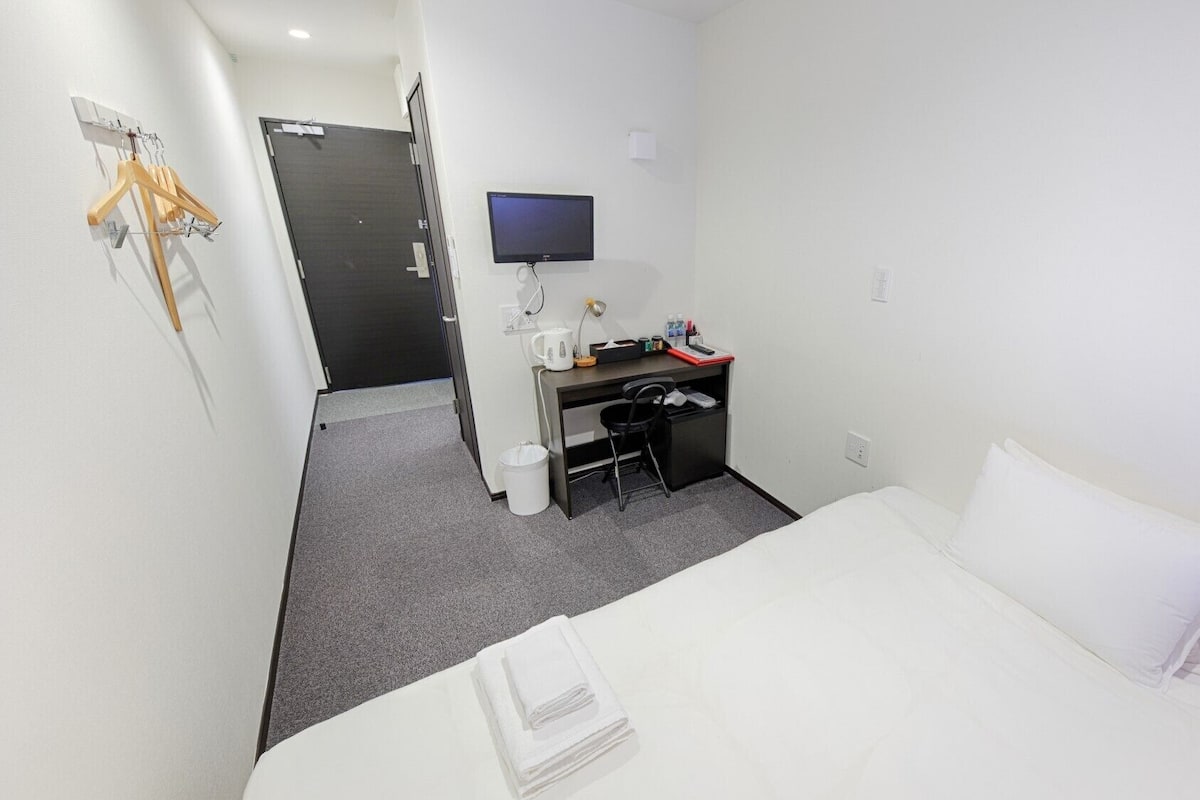 Ein Hotelzimmer mit Bett, Schreibtisch, Stuhl, Fernseher und Kleiderhaken.