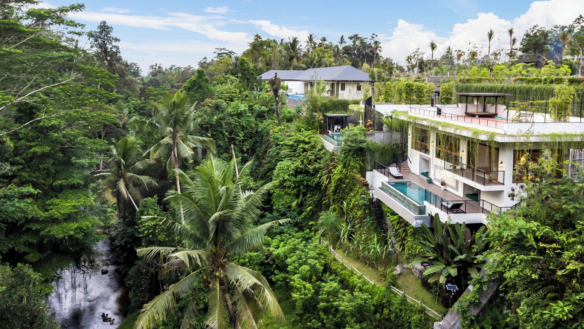 Une villa moderne dotée d’une piscine, entourée d’une végétation tropicale luxuriante et d’une cascade.