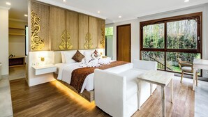 Une chambre d’hôtel moderne dotée d’un grand lit, d’un coin salon avec une table et offrant une vue sur la verdure grâce à de grandes fenêtres.