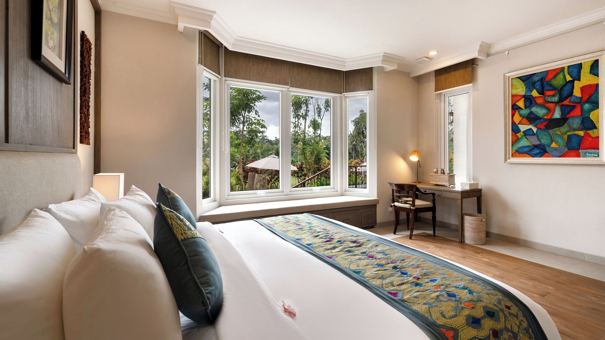 A hotel room with a bed, a desk, and a large window offering a view of the outdoors.